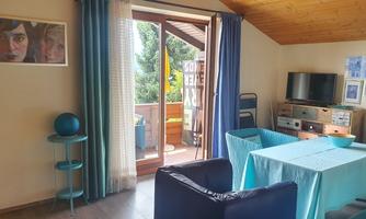A cozy living space with a table and chairs in shades of blue. There is a balcony with an outdoor view and a TV corner.