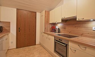 A modern kitchen with light cabinets and wooden cladding.  
It is well-equipped and has an inviting atmosphere.