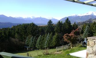 A serene landscape with mountains in the background and green forests in the foreground. The clear sky creates a peaceful atmosphere.