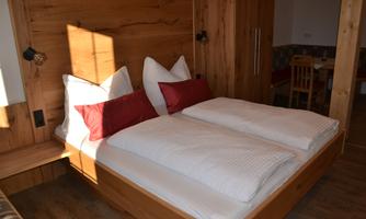 A cozy bedroom with a double bed and red pillows. The bright wooden wall and warm light create an inviting atmosphere.