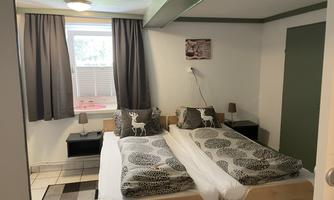 A cozy bedroom with two single beds and gray curtains. There are nightstands and a window that provides natural light.