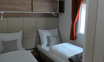 A simple bedroom with two beds and a window. Orange curtains and modern furnishings create a cozy atmosphere.