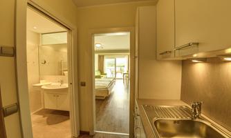 A modern kitchen with a sink and direct access to a bright bathroom as well as a living area. The space is well-lit and designed to be friendly.