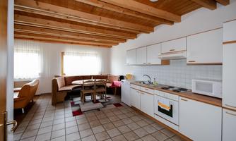 A bright and modern kitchen with wooden ceiling beams. It is equipped with a dining table, chairs, and modern appliances.