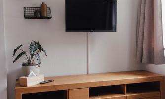 A modern living space with a low wooden cabinet and a television on the wall. A vase with a plant is on the table, and the room is not lacking in natural light.