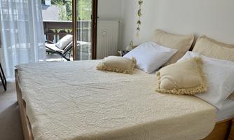 A cozy bedroom with a large bed and soft pillows. The windows open to a balcony with a view of nature.