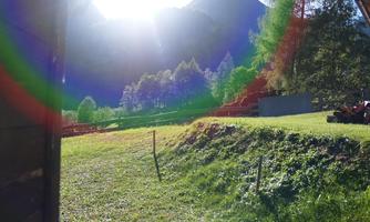 A picturesque landscape with green meadows and mountains in the background. The sun is shining brightly, creating a beautiful light effect.