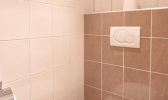 A modern, clean restroom with a white toilet and a wall tiled in brown. The surroundings are bright and minimally designed.
