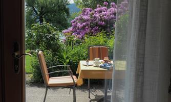 A cozy table with two chairs outside, surrounded by colorful flowers. On the table, cups and small snacks are prepared.