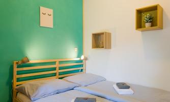A modern bedroom with a wooden bed and a mint green wall. Fresh towels are on the bed, and there are decorative elements on the wall.