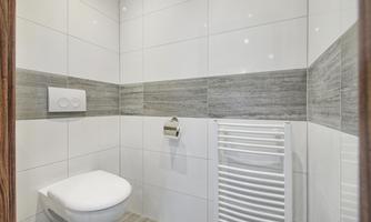 A modern bathroom with white tiles and gray accents. It includes a toilet, a towel holder, and a wall heater.