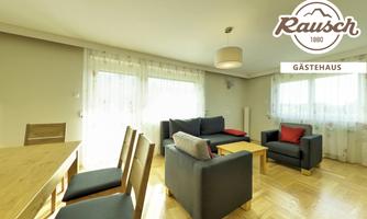 A cozy living room with a comfortable sofa and chairs. Bright windows provide plenty of daylight.