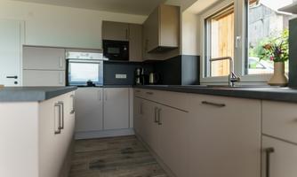 A modern kitchen with light cabinets and an elegant countertop. Large windows provide plenty of daylight.