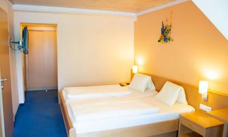 A simple bedroom with two single beds and warm colors. There is a desk and a wardrobe, as well as a TV unit on the wall.