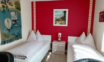 A cozy bedroom with two single beds and red walls. A decorative wall tapestry with swans hangs on the wall.