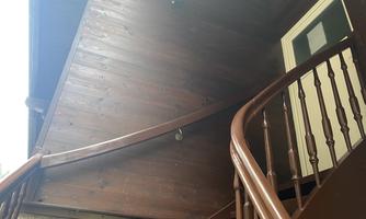 A wooden staircase leads to the door of a wooden house. The wall is vertical and clad with wooden panels.