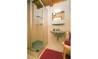 A modern bathroom with a shower and a washbasin. The walls are brightly tiled and there is a warm carpet floor.