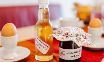 A set table with two soft-boiled eggs, a bottle of vinegar, and a glass of jam. The jam is covered with a colorful cloth and labeled.