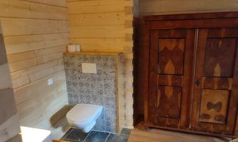 A cozy bathroom with wood paneling and a modern toilet. A rustic cabinet complements the warm atmosphere.