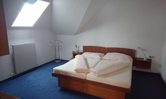 A bright bedroom with a double bed and two nightstands. A window with a sloping roof provides daylight.