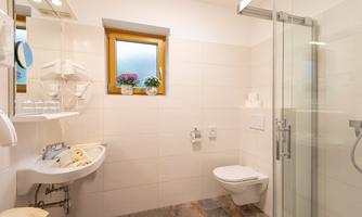 A modern bathroom with a shower and a sink. The walls are decorated in light colors, and flowering plants are on the windowsill.