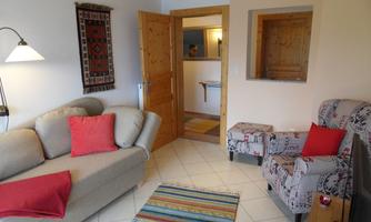 A cozy living room with a bright sofa and two chairs. The room has a warm wood look and an inviting atmosphere.