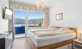 A modern bedroom with a large window and a view of the lake. There is a double bed, a dresser, and a television.