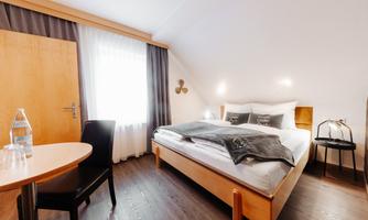 A cozy bedroom with a large bed and a round table. The room has bright curtains and a modern wooden floor.