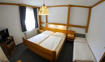 A cozy hotel room with a large double bed and an additional single bed. The walls are light and decorated with a wood design.