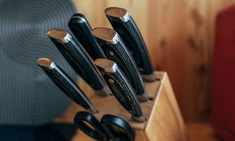 A stylish wooden knife block with several black knives. In the background, kitchen details are visible.