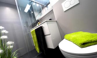 A modern bathroom with a glass shower and an elegant sink. On the toilet, there is a green towel next to a black one and a light-colored one.