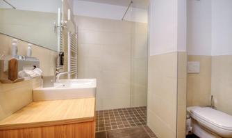 A modern bathroom with a shower, a sink, and a toilet. The walls are in light colors, and the floor is tiled.