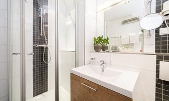 A modern bathroom with a walk-in shower and an elegant sink. Decorative plants and bright tiles add freshness to the space.