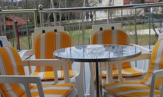 A balcony with modern white chairs and a round table. The chairs have yellow and white stripes, and there is a glass vase on the table.
