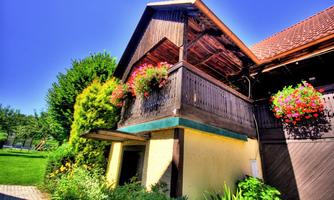 A charming building with a balcony decorated with colorful flowers. In the foreground, lush plants and a well-kept lawn can be seen.