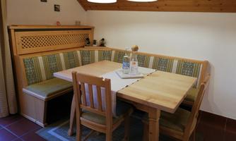 A cozy dining area with a wooden bench and a large table. The room has a warm atmosphere with a wooden ceiling and decorative elements.