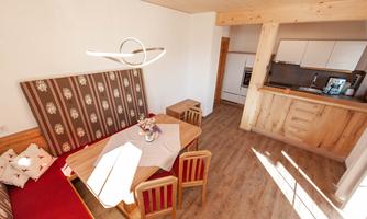A cozy living area with a wooden kitchen and a dining area. The warm colors and wooden details create an inviting atmosphere.