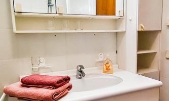 A modern bathroom with a sink and a mirror. Red towels are placed on the shelf, and there is a small cabinet.