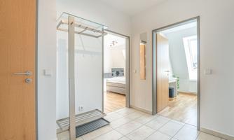 A bright hallway with modern tiles and a shoe rack. To the right, a door leads to another room.