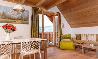 A cozy living space with a dining table and white chairs. Large windows offer a view of nature and let in plenty of light.