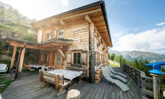 A charming wooden house in the mountains with an inviting terrace. Through the windows, one looks out at a picturesque mountain landscape.