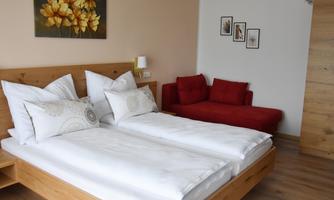 A modern bedroom with two separate beds and white bedding. The room features a red sofa and a painting on the wall.