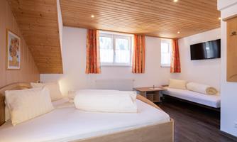 A cozy room with a wooden ceiling and window. There are two beds and a TV on the wall.
