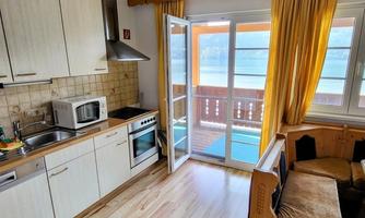 A bright kitchen with modern appliances and wooden shelves. The windows open to a beautiful balcony overlooking the water.