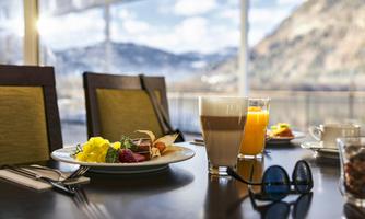 A lovingly set breakfast table with a selection of dishes, including fruits and pastries. In the background, a beautiful view of the landscape is visible.