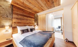 A cozy bedroom with wooden decor and modern furnishings. The bed is outfitted with soft pillows and a warm blanket.