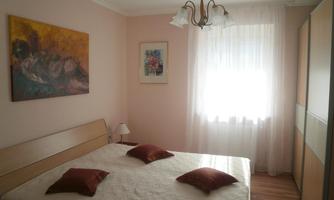 A cozy bedroom with a double bed and decorative pillows. Pictures hang on the wall and the window lets in plenty of light.