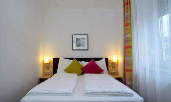 A cozy bedroom with a large bed and colorful pillows. Soft lighting and a window create an inviting atmosphere.
