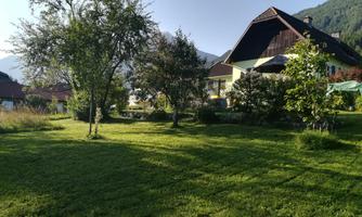 A beautiful house surrounded by green meadows and trees. In the background, mountains can be seen.