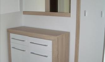 A modern hallway with a light-colored wooden cupboard and a mirror. There are storage options for coats and bags hanging on the wall.